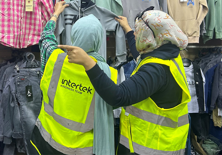 Two women in headscarves and Intertek branded worker vests browse children's clothing