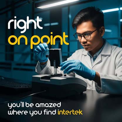 A technician in a lab coat examining a vial of dark liquid next to a machine